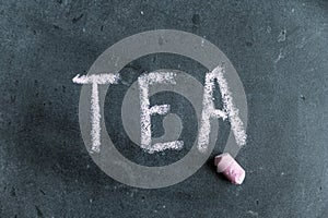Tea. A word written in pink chalk on a black chalkboard. Handwritten text. A piece of colored chalk hangs next to it