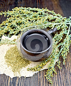 Tea with wormwood in cup on dark board