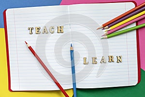 Teach and learn, words in open notebook, colorful crayons and colored paper sheets. Concept of education, starting