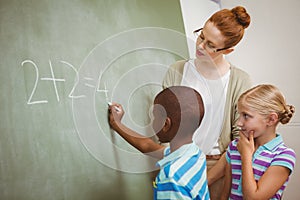 Teacher assisting boy to write on blackboard in classroom