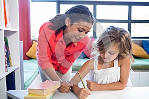 Teacher assisting girl writing on notebook in library