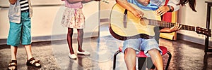 Teacher assisting a kids to play a musical instrument in classroom