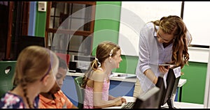 Teacher assisting school kids on personal computer in classroom