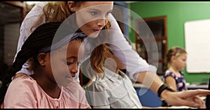 Teacher assisting school kids on personal computer in classroom