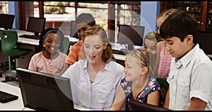 Teacher assisting school kids on personal computer in classroom