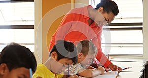 Teacher assisting school kids with their classwork in classroom