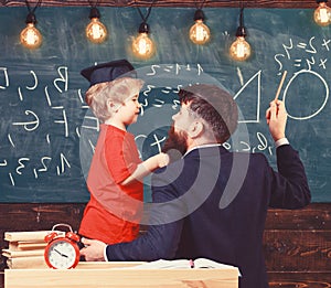 Teacher with beard, father teaches little son in classroom, chalkboard on background. Instructive conversation concept photo