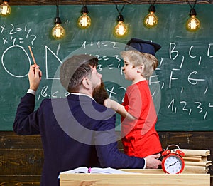 Teacher with beard, father teaches little son in classroom, chalkboard on background. Instructive conversation concept photo
