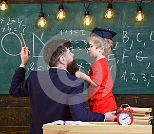 Teacher with beard, father teaches little son in classroom, chalkboard on background. Instructive conversation concept