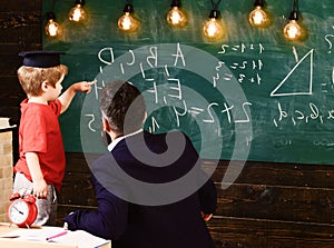 Teacher with beard, father teaches little son in classroom, chalkboard on background. Prodigy child concept. Boy, child