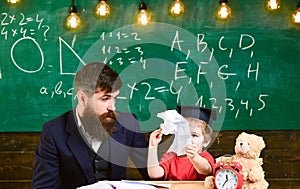 Teacher with beard, father teaches little son in classroom, chalkboard on background. Tries and mistakes concept. Boy