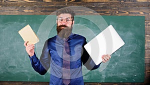 Teacher bearded hipster holds book and laptop. Choose right teaching method. Modern instead outdated. Teacher choosing