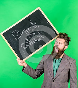 Teacher bearded man holds blackboard with inscription back to school green background. Teacher with tousled hair