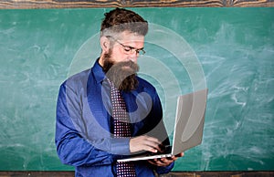 Teacher bearded man with modern laptop chalkboard background. Online education. Modern technology education. Hipster