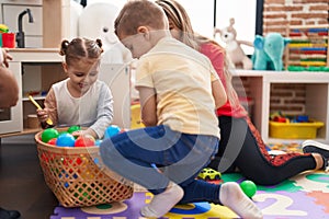 Teacher with boy and girl playing with balls sitting on floor at kindergarten