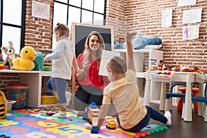 Teacher with boy and girl sitting on floor having maths lesson at kindergarten