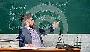 Teacher charismatic hipster sit at table classroom chalkboard background. Educational conversation. Talking to students