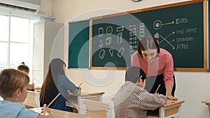 Teacher checking cute student homework while explaining idea at class. Pedagogy.
