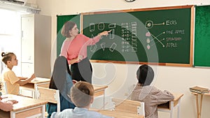 Teacher checking cute student homework while explaining idea at class. Pedagogy.