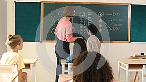 Teacher checking cute student homework while explaining idea at class. Pedagogy.