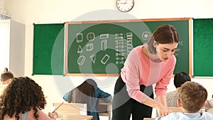 Teacher checking cute student homework while explaining idea at class. Pedagogy.