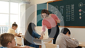 Teacher checking cute student homework while explaining idea at class. Pedagogy.