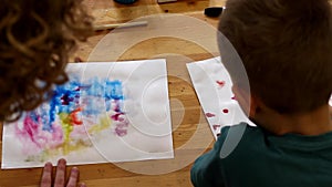 The teacher and the child draw with pencil on paper in art classes. Hands on the table top view. Children`s workshop