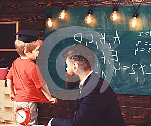 Teacher and child talking in the classroom. Little schoolboy in Oxford cap answering the question in front of the green