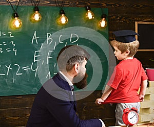 Teacher and child talking in the classroom. Little schoolboy in Oxford cap answering the question in front of the green