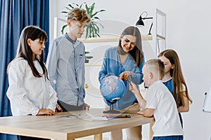 Teacher and children in class are looking at globe, teacher helps explain the lesson to the children in the class at a desk