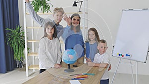 Teacher and children in class are looking at globe, teacher helps explain the lesson to the children in the class at a desk.