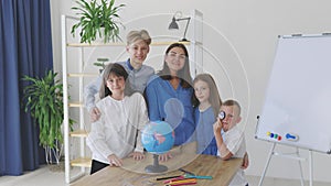 Teacher and children in class are looking at globe, teacher helps explain the lesson to the children in the class at a desk.