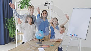 Teacher and children in class are looking at globe, teacher helps explain the lesson to the children in the class at a desk.