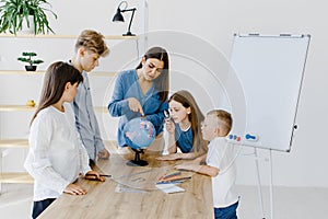 Teacher and children in class are looking at globe, teacher helps explain the lesson to the children in the class at a desk