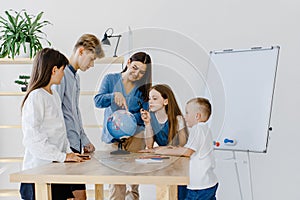 Teacher and children in class are looking at globe, teacher helps explain the lesson to the children in the class at a desk