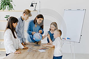 Teacher and children in class are looking at globe, teacher helps explain the lesson to the children in the class at a desk