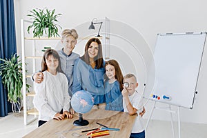 Teacher and children in class are looking at globe, teacher helps explain the lesson to the children in the class at a desk