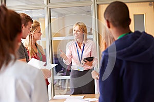 Teacher With College Students Standing By Desks In Classroom