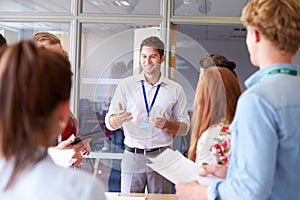 Teacher With College Students Standing By Desks In Classroom