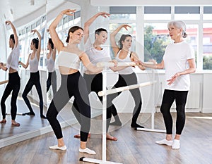 Teacher conducts class with girls in ballet studio, observes doing grand plie exercise.