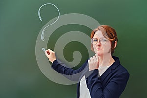 Teacher drew a question mark in chalk on a blackboard, copy space on green background. Woman teacher with a sad face at the school