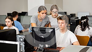 Teacher explaining task solution to young girl and boys during computer science lesson