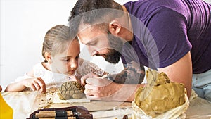 Teacher explains and shows his pupil girl how to modeling a toy from clay.