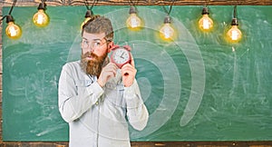 Teacher in eyeglasses holds alarm clock. Man with beard and mustache on concentrated face listening clock. Bearded