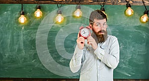 Teacher in eyeglasses holds alarm clock. Man with beard and mustache on concentrated face listening clock. School bell