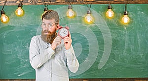 Teacher in eyeglasses holds alarm clock. Man with beard and mustache on concentrated face listening clock. School bell