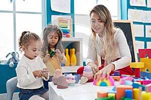 Teacher with girls playing with geometry blocks sitting on table at kindergarten