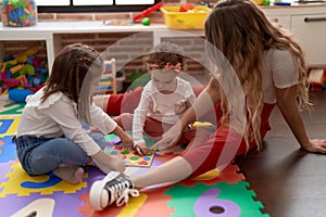 Teacher with girls playing with maths puzzle game sitting on floor at kindergarten