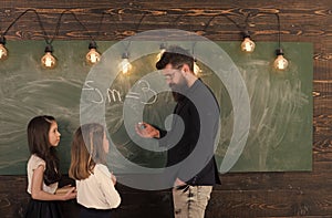 Teacher and girls pupils in classroom near chalkboard. Curious concentrated children listening teacher with attention