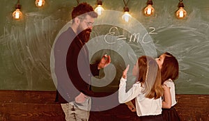 Teacher and girls pupils in classroom near chalkboard. Man with beard in formal suit teaches schoolgirls physics